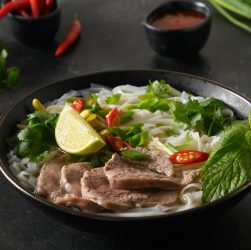 Pho Bo Soup with beef, rice noodles, lime, chili pepper in black bowl. Vietnamese cuisine.