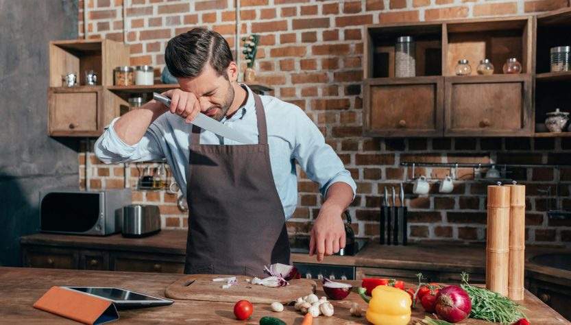 young man crying while cutting onion